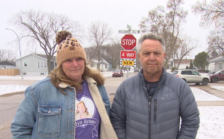 Two people besides a snowy intersection on a residential street.