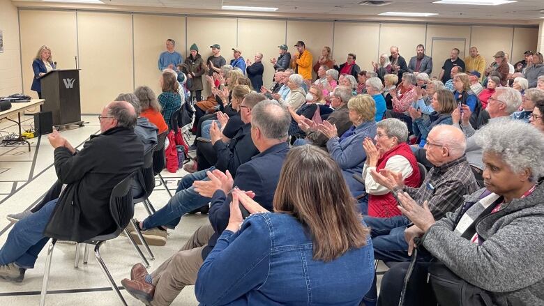 A room full of clapping people at a town hall meeting. 