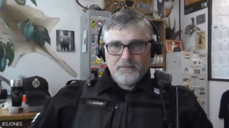 A man sits at a desk in an office wearing a uniform similar to a police officer. He had headphones on.