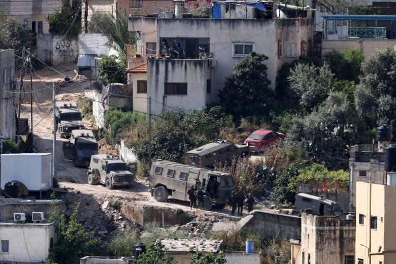 A line of military vehicles are seen parked on a hillside road.