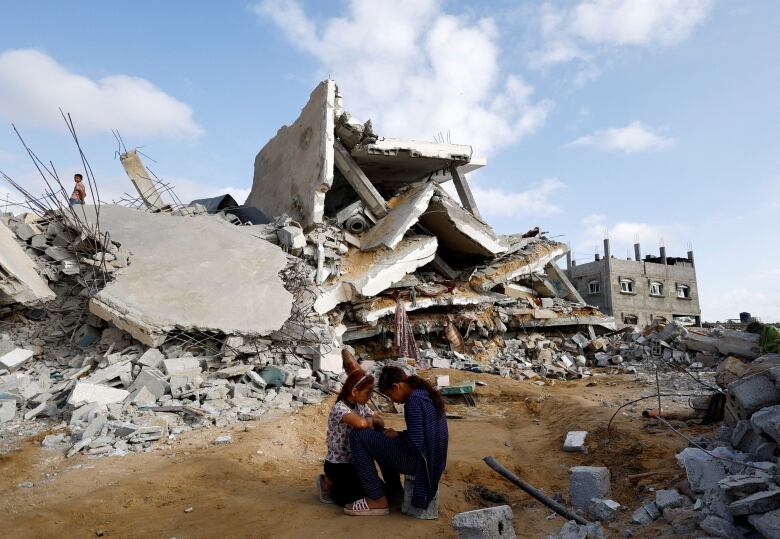 Children huddle and sit next to the debris of a destroyed building.