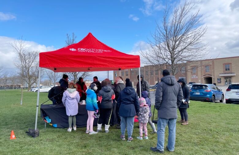 Crowd of people stand near red tent that says 