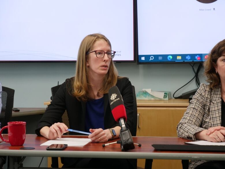 A woman speaks at a desk with a microphone in front of her