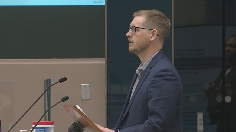 a man in a suit with glasses speaks into a microphone at a podium.