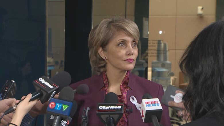 a woman in a suit jacket stands in front of many microphones.