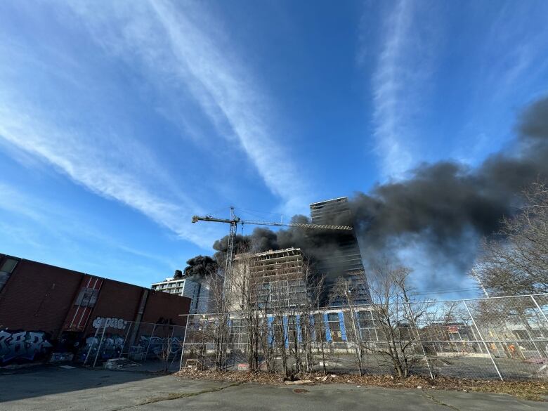 Black smoke is seen billowing from a building under construction with a crane next.