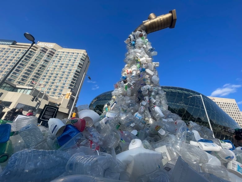 A pile of plastic bottles appears to float out of a tap floating in the air, with buildings in the background.