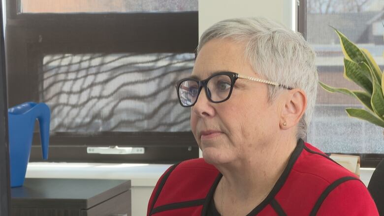 Woman with glasses and short grey hair dressed in red and black suit.