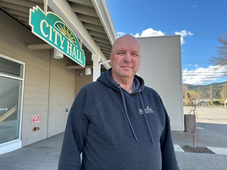 A man wearing a grey hoodie stands in front of a sign that says City Hall