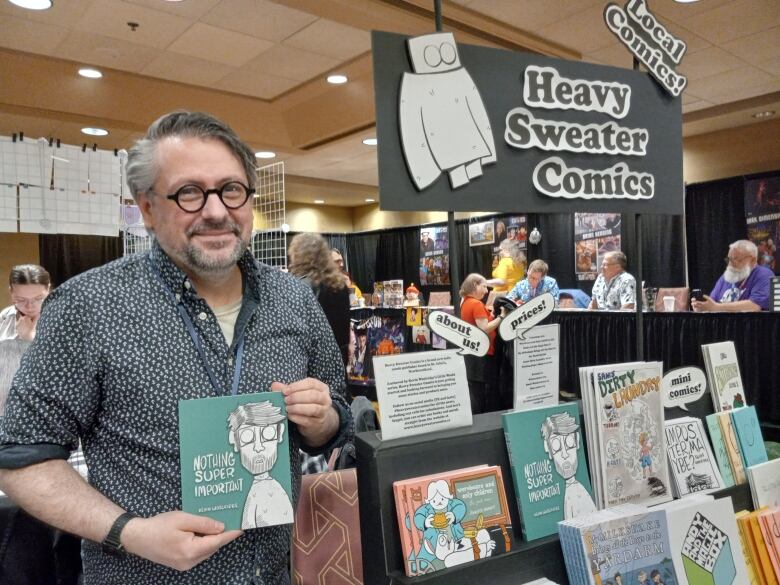 Man in short sleeve dress shirt standing next to stack of comic books