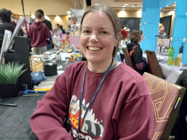 Woman with shirt blond hair sitting down and smiling in burgundy sweater