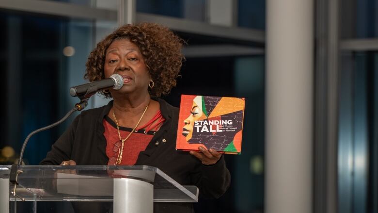 A person standing at a podium holds the book Standing Tall