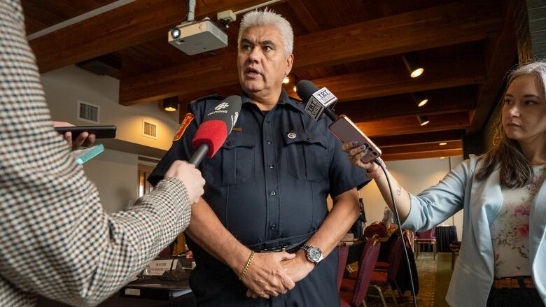 A person wearing a police uniform stands in between two people holding microphones to his face.