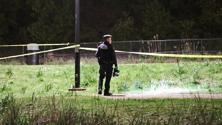 A police officer with a camera is pictured at night near yellow crime tape.