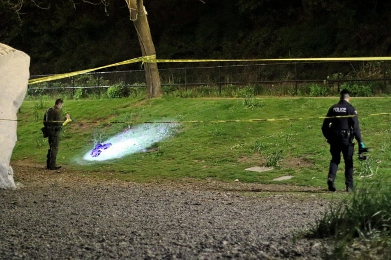 Police behind yellow crime tape look at a piece of cloth on a grassy hill.