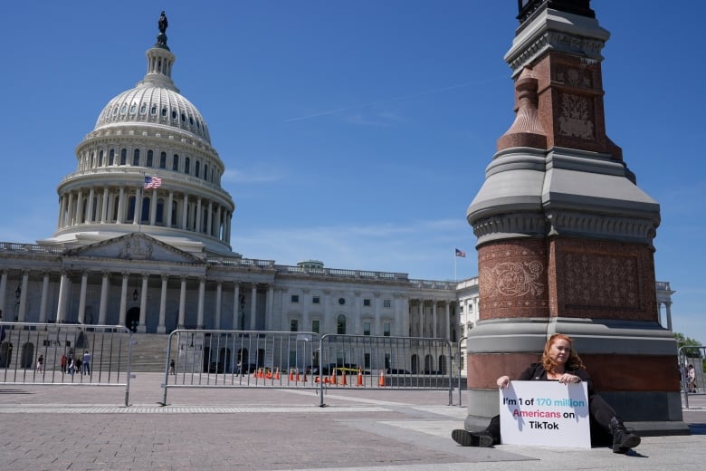 Woman in front of Capitol Dome holds sign saying: 