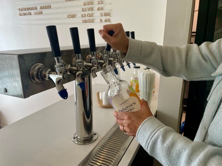 Two hands work the taps of a drink dispenser, filling up a bottle with the label Parkerview Brews visible on the label.