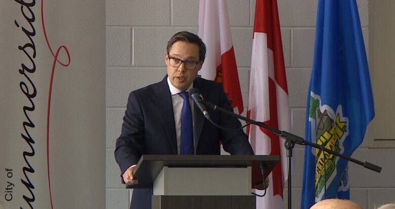 A man with short dark hair, glasses and a suit speaks at a podium in front of a City of Summerside sign.