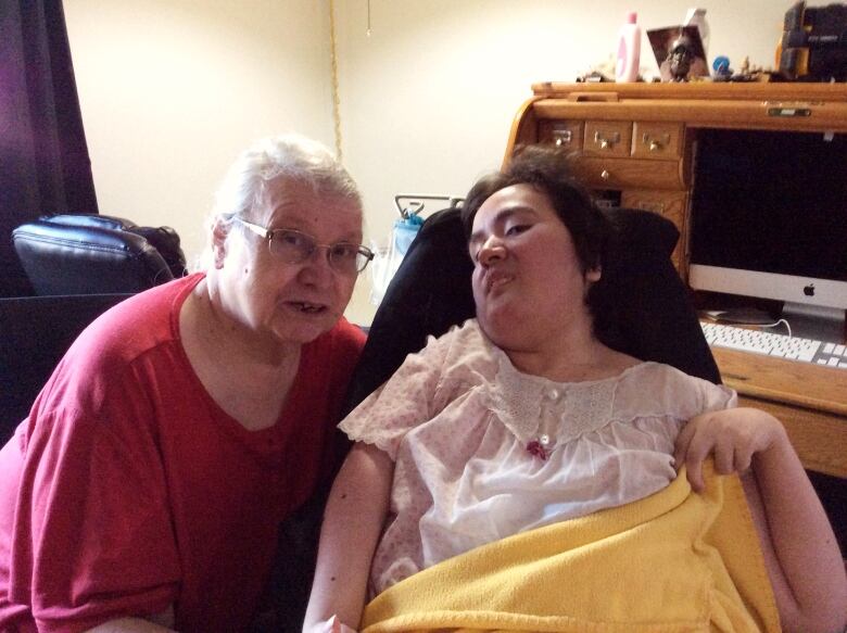 An older woman and a younger woman sit side-by-side inside a home.