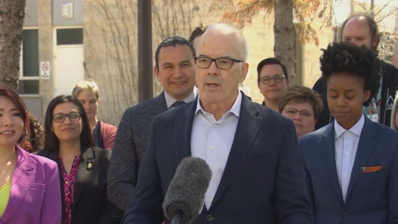 A man speaks into a microphone surrounded by a crowd of people.