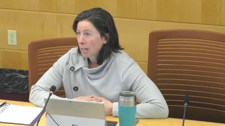 A woman speaks at a microphone at a desk 