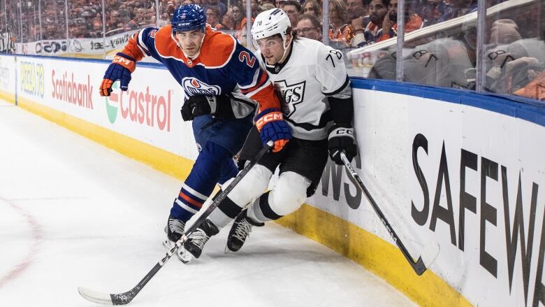 One hockey player body-checks another against the glass.