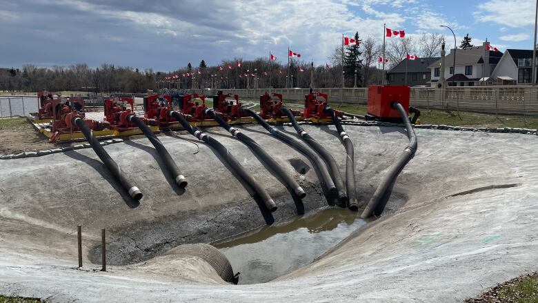 A cement pad is partially filled with water. On the side of the cement pad are a series of large hoses connected to orange machinery. 