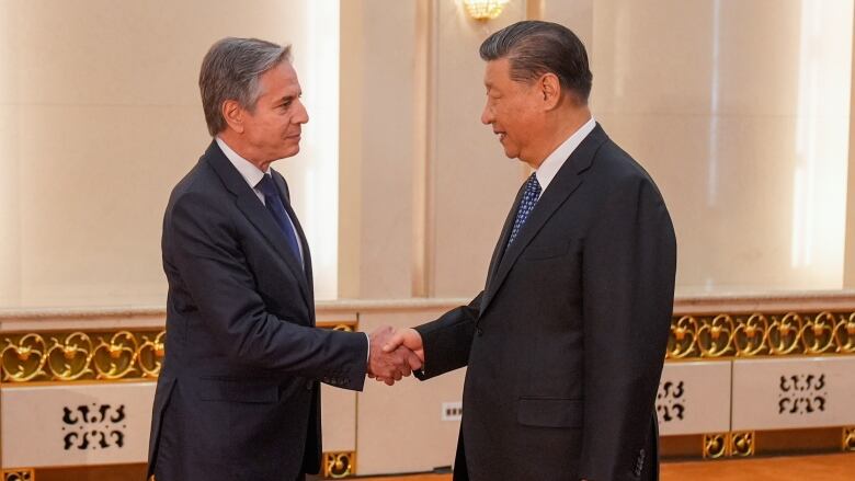 Two men in suit and ties, one Caucasian and one Asian, shake hands while standing in a room.