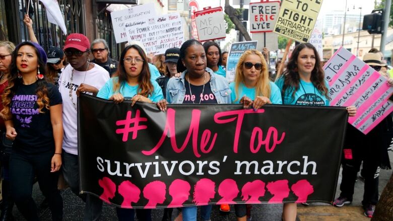 Women march holding a banner that says #MeToo survivors march