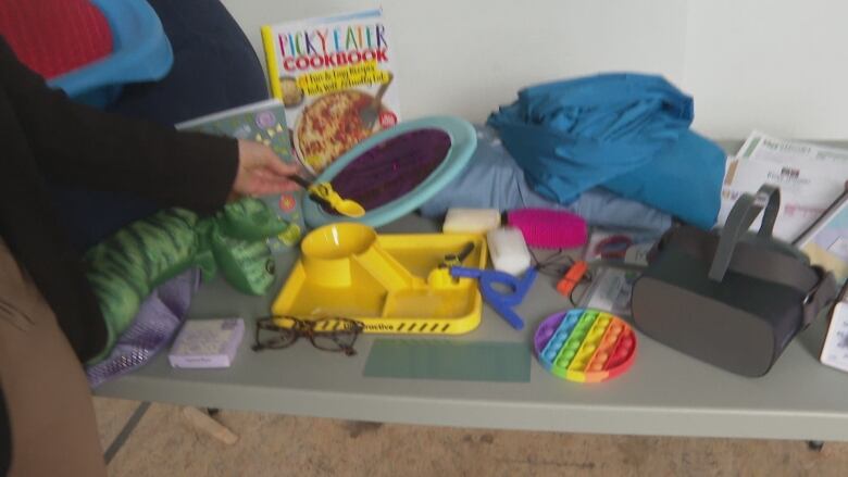 A hand holds a yellow plastic spoon over a table pull of toys.