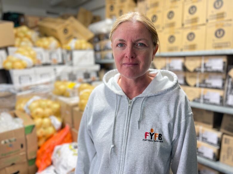 A woman wearing a grey zip-up hoodie stands in a food bank.