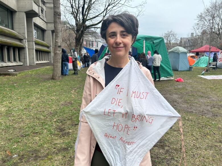 A woman with short grey hair holds up a white kite that says 