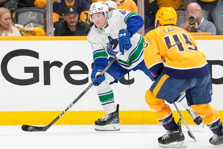 A hockey player shoots the puck with another opponent approaching.