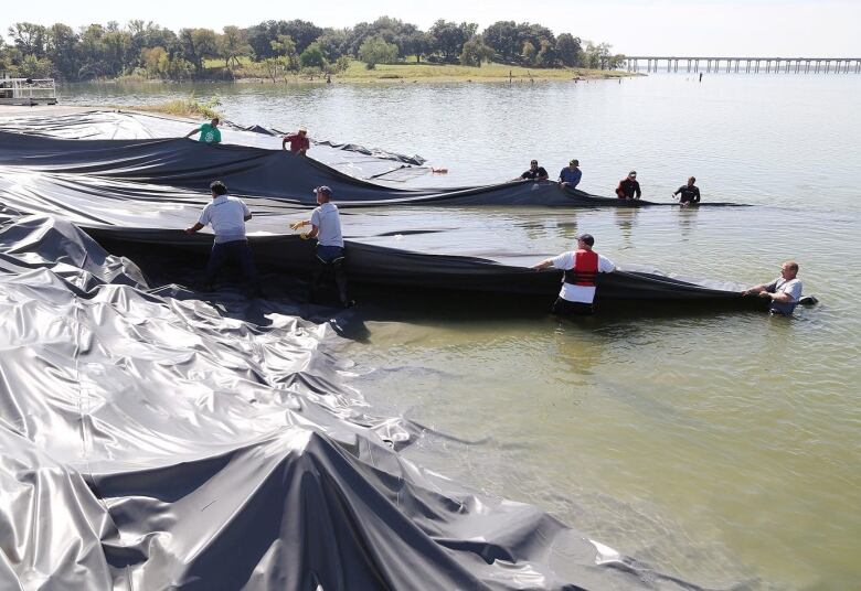 People pull a large black tarp into a lake