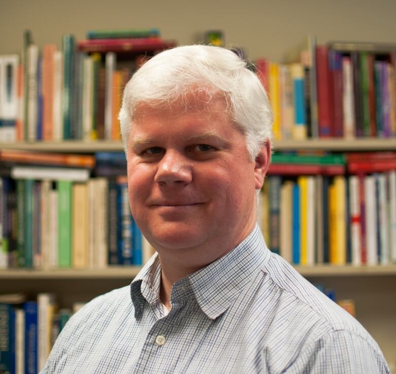 Man with grey hair standing in front of bookshelf.