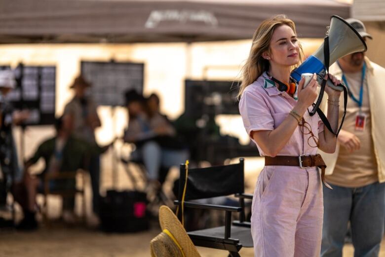 A woman in a jumpsuit who plays a director, holds a megaphone