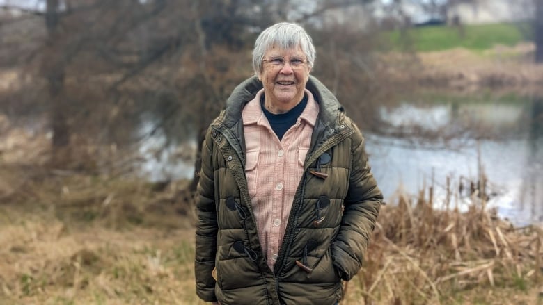 A woman in a green jacket stands near a pond 