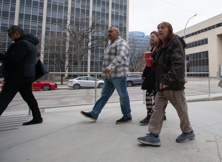 A group of people walk next to a street lined by buildings.