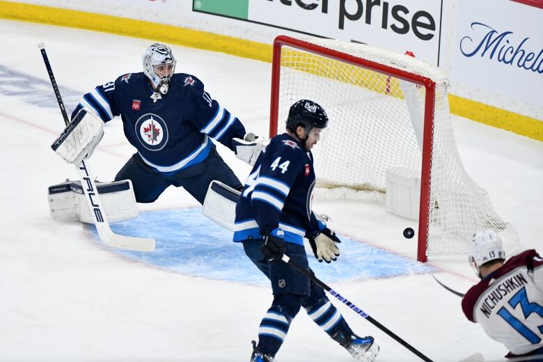 A Colorado player shoots into an open net while Winnipeg's goaltender and a defenceman try in vain to block the shot.