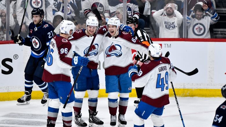 Four Colorado Avalanche players celebrate a goal, while fans behind the glass react.