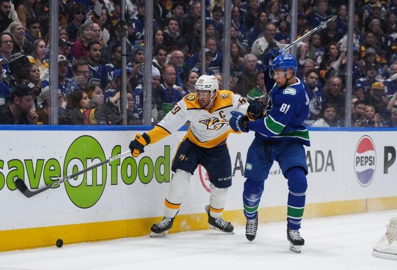 A hockey player in blue and green grabs the jersey of another player in yellow and white on the ice as they both fight for the puck.