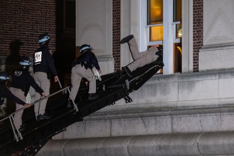 Police officers in helmets are shown climbing a ladder to gain entry inside a stone building.