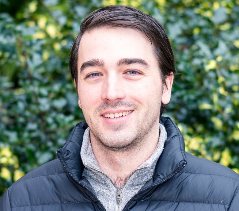 A smiling man in front of a bush