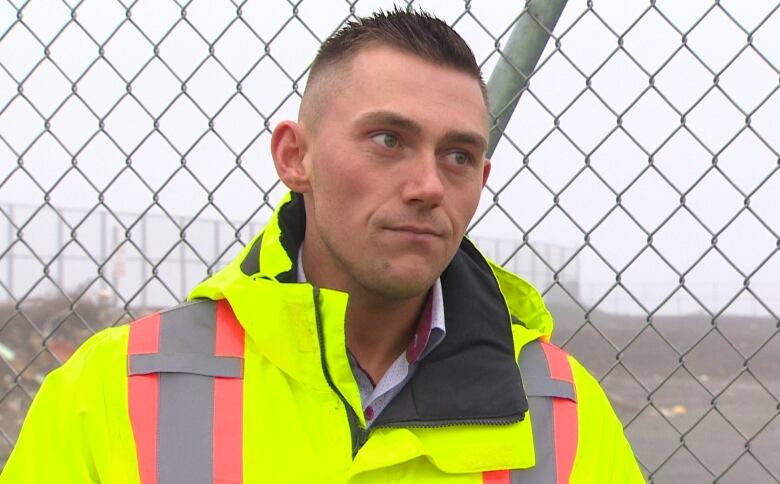 A man in a yellow jacket standing near a chain link fence. 