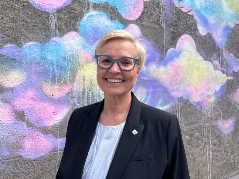 A woman smiling at the camera against a colourful chalk graffiti background. 