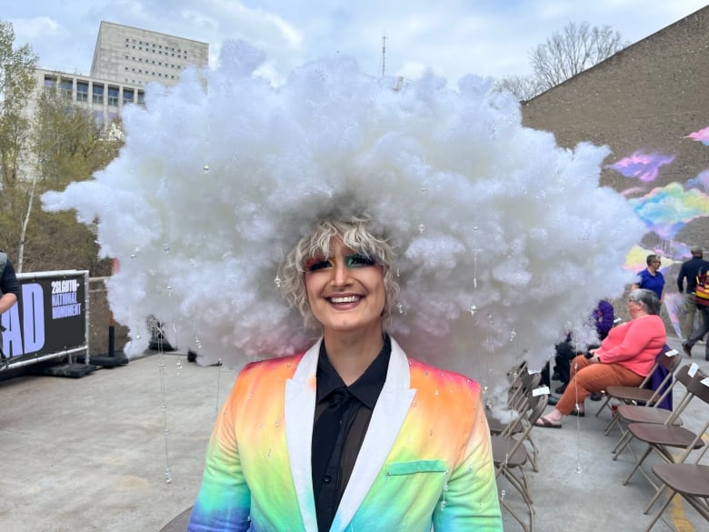 A man wearing a rainbow suit and a decorative cloud on his head.