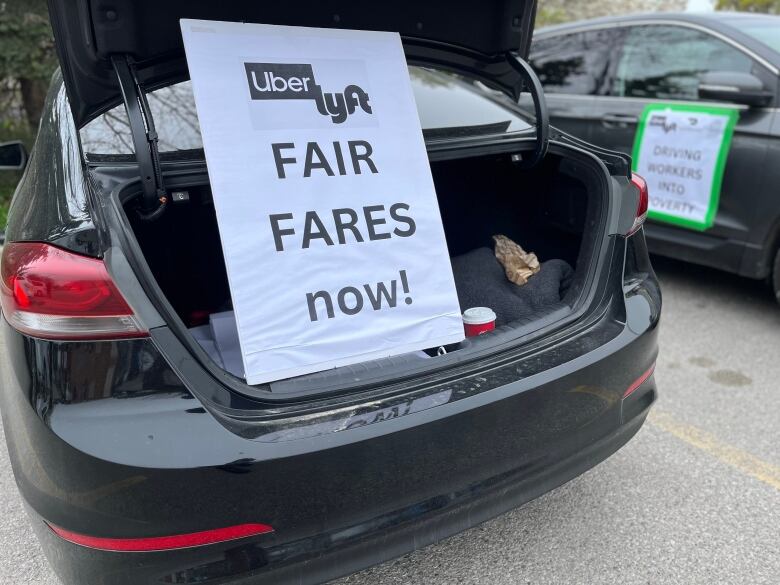 A sign in the open trunk of a parked black car reads 