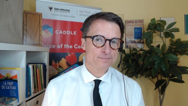 A man wearing a white dress shirt and black tie speaks into a headset on a Zoom call.