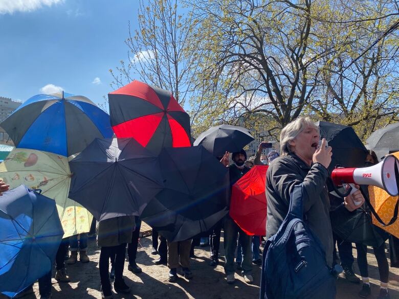 A wall of umbrellas and a man with grey hair and a loud speaker a man holds a peace sign with his fingers behing an umbrella