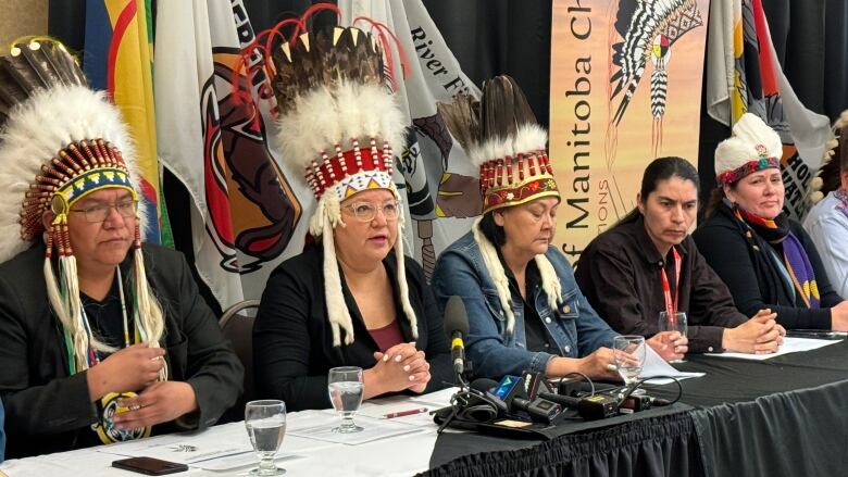 Five people, including four wearing headdresses, sit at a long conference table.